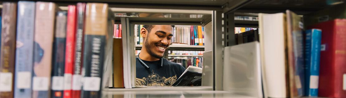 A student smiles while looking at a book in a Pima campus Library